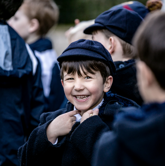 Little boy in school uniform in a crowd turning round smiling