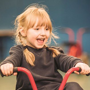Tot with pigtail plaits playing on tricycle